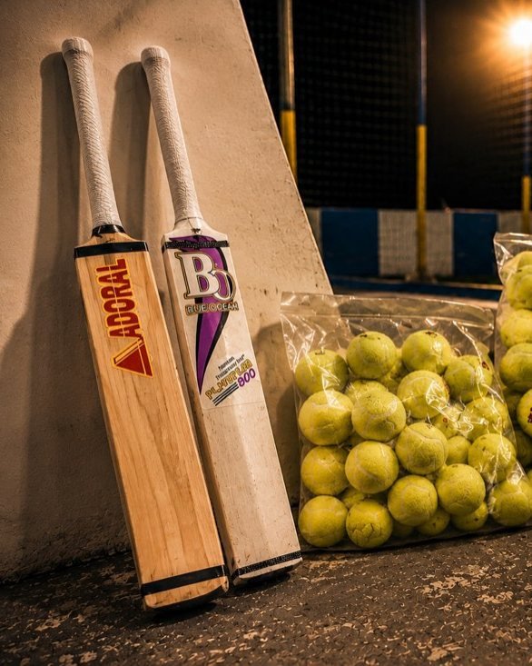 Two bats propped against the wall next to bags of tape balls