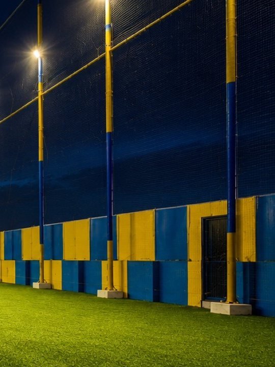 Floodlight poles and the blue and yellow padded wall along the netted side