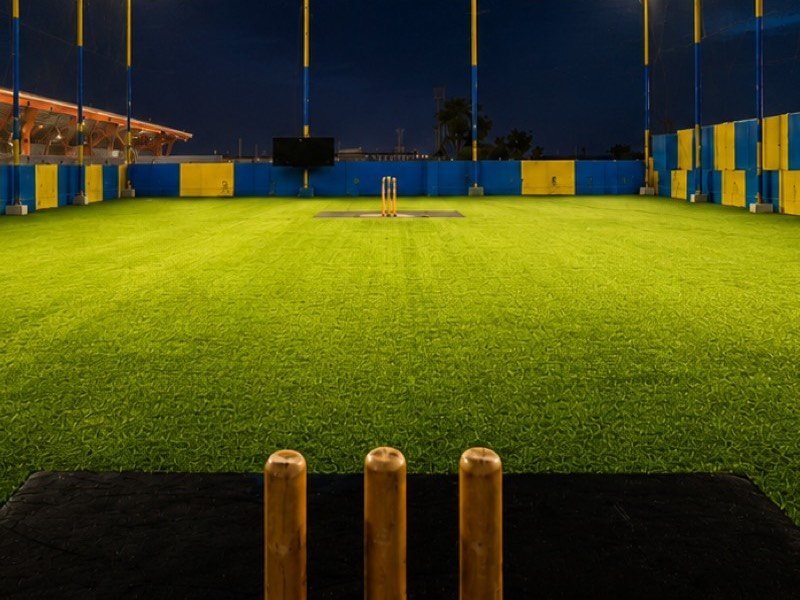 Stumps at the batting end with the pitch stretching away under the lights